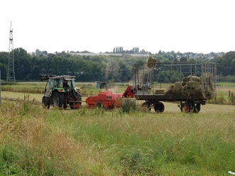 NSG Füllenbruch Ein Traktor zieht eine Heupresse über ein Feld, während ein großer Anhänger mit gepresstem Heu beladen wird.