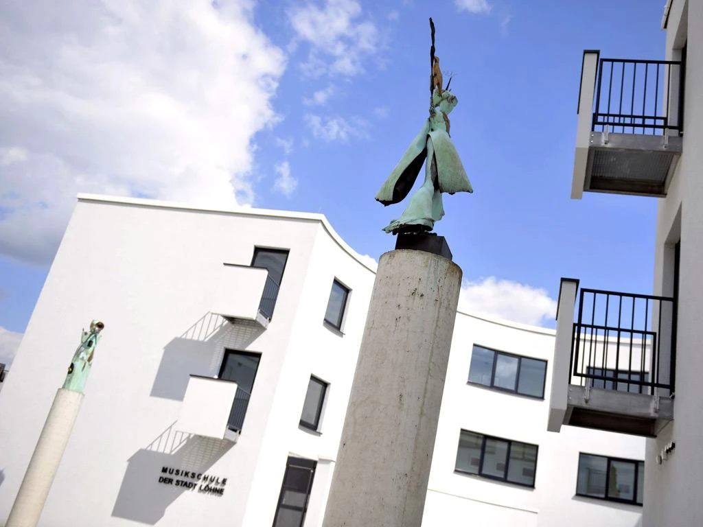 Skulpturen auf Säulen vor modernem, weißem Gebäude der Musikschule Löhne an einem sonnigen Tag.