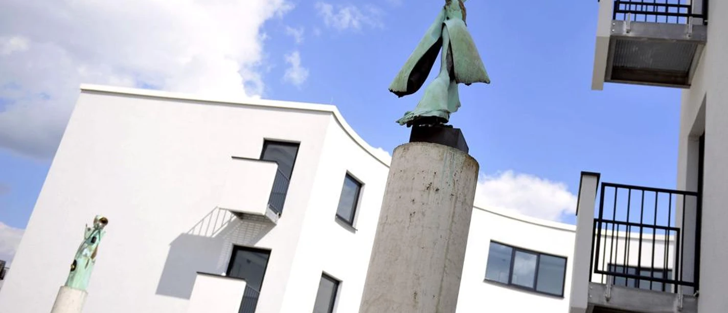 Skulpturen auf Säulen vor modernem, weißem Gebäude der Musikschule Löhne an einem sonnigen Tag.