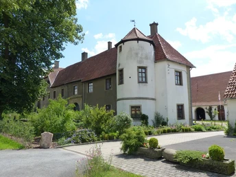 Ein historisches Gebäude mit Rundturm, umgeben von gepflegten Grünflächen und blühenden Pflanzen.
