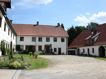 Historisches Gebäude mit zwei Flügeln, begrüntem Innenhof, Kiesweg und Blumenarrangements.
