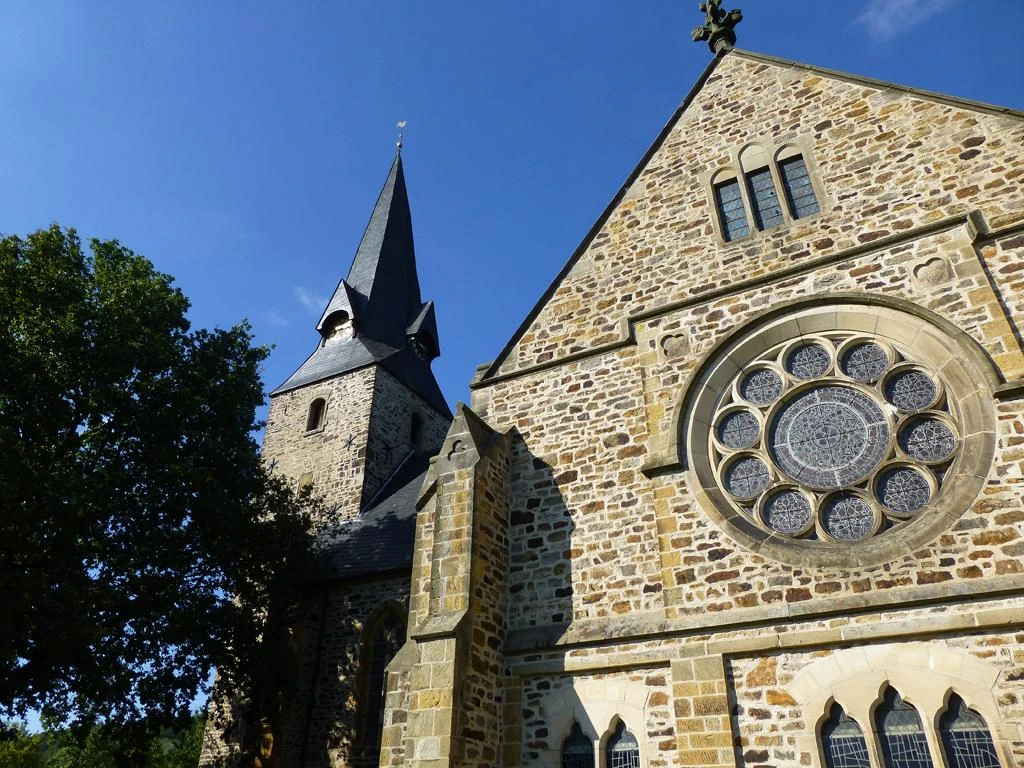 Romanische Kirche St. Bartholomäus mit markantem Glockenturm und beeindruckendem Rundfenster.