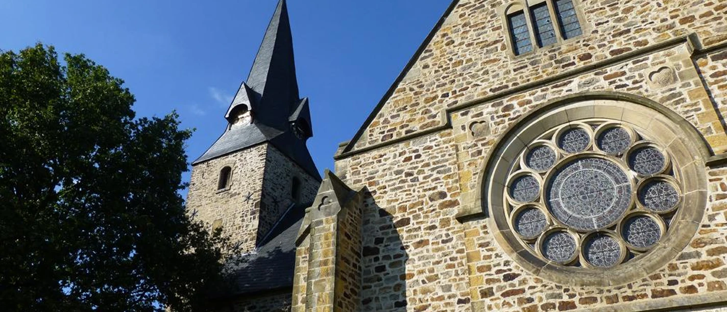 Romanische Kirche St. Bartholomäus mit markantem Glockenturm und beeindruckendem Rundfenster.
