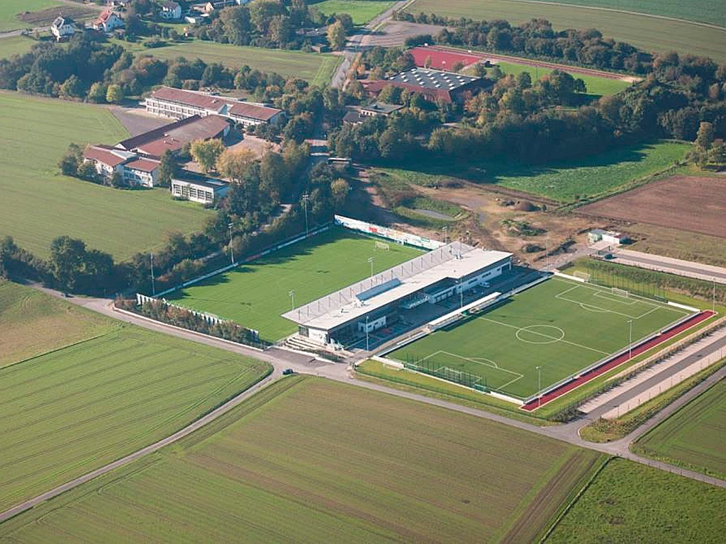 Luftaufnahme des Häcker Wiehenstadions, umgeben von Feldern und Gebäuden in einer ländlichen Umgebung.