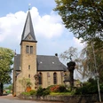 Historische Michaelkirche aus Backstein mit hohem Turm, umgeben von Bäumen und gepflegtem Garten.