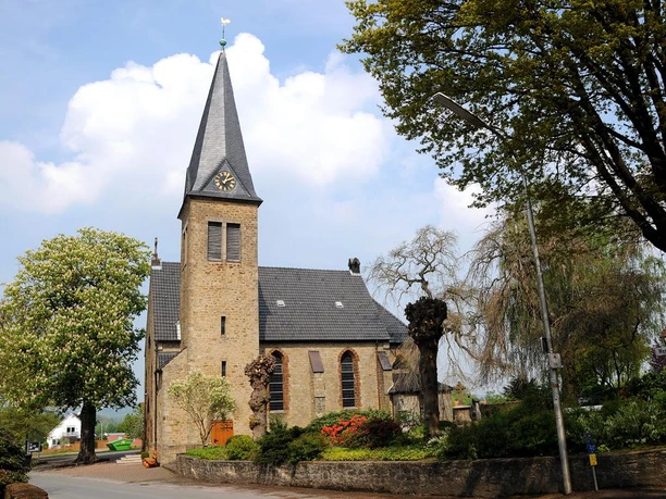 Historische Michaelkirche aus Backstein mit hohem Turm, umgeben von Bäumen und gepflegtem Garten.