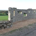 Steinerne Mauer mit Fensteröffnungen auf einem Naturerlebnispfad, umgeben von grünen Feldern.