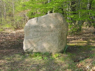 Gedenkstein für den Dichter Rainer Maria Rilke mit Inschrift, umgeben von Bäumen und Waldboden.