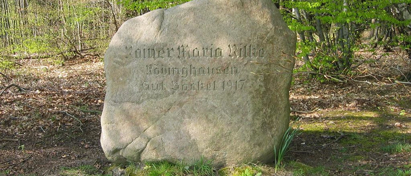 Gedenkstein für den Dichter Rainer Maria Rilke mit Inschrift, umgeben von Bäumen und Waldboden.