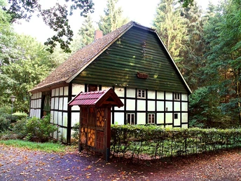 Katzenholz - Hühnerhaus Fachwerkhaus im Grünen, umgeben von Bäumen, mit Schindeldach und dekorativem Holzportal im Vordergrund.