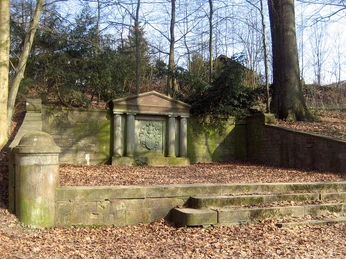 Steingrab mit Ritterwappen im winterlichen Wald, umgeben von grün bemoosten Stufen und Bäumen.