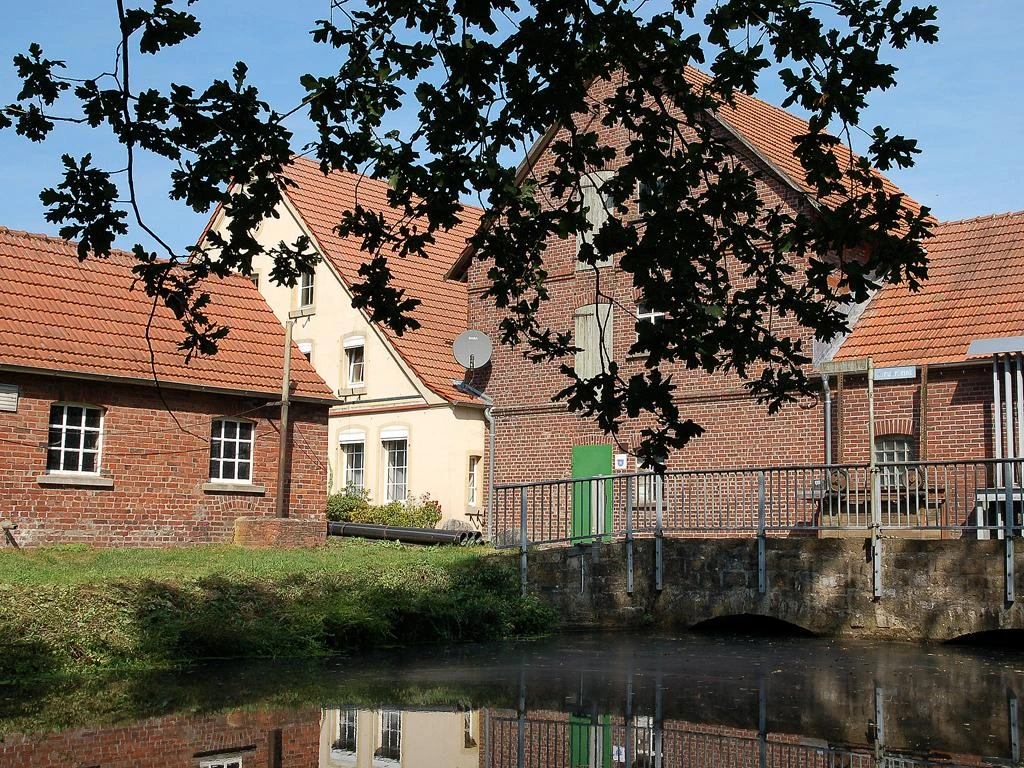 Historische Martmühle mit roten Ziegeldächern, von Bäumen umrahmt, an einem kleinen Gewässer.
