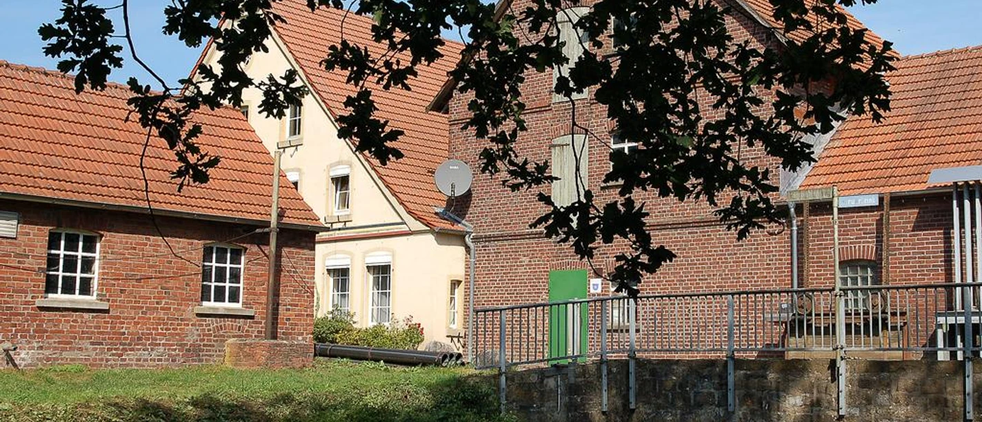 Historische Martmühle mit roten Ziegeldächern, von Bäumen umrahmt, an einem kleinen Gewässer.