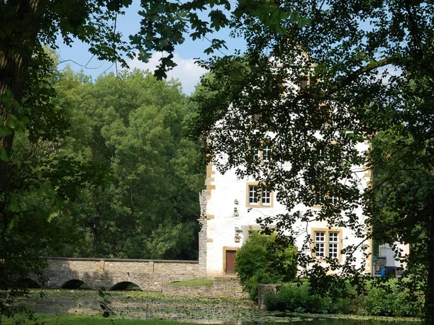 Schloss Königsbrück umgeben von üppigem Grün, mit einer Steinbrücke über einen stillen Wassergraben.