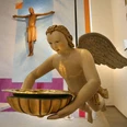 Taufengel in der Kirche Valdorf Ein Taufengel schwebt im Kirchenraum, hält eine Schale; im Hintergrund ein Kruzifix zu sehen.