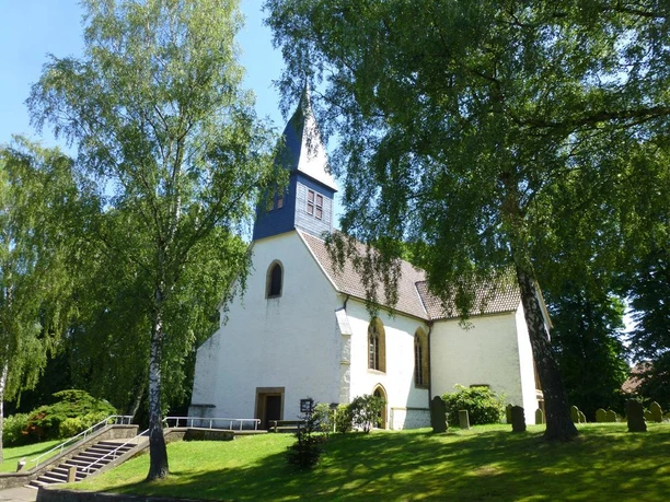 Valdorfer Kirche Einsame Kirche mit spitzem Turm umgeben von Bäumen, situiert in einer grünen, friedlichen Umgebung.