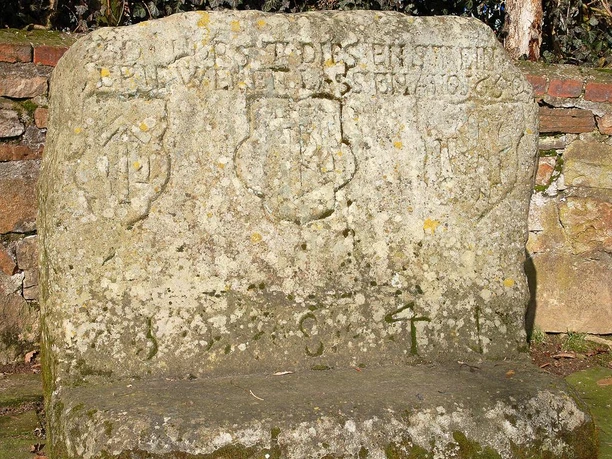 Gravierte Steinplatte mit historischen Wappen und Inschriften, umgeben von einer steinernen Mauer.