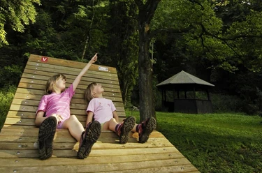 Das Kombiskop befindet sich direkt an einer Schutzhütte und Liegebank Zwei Kinder sitzen auf der Liegebank im Arboretum Bad Driburg.