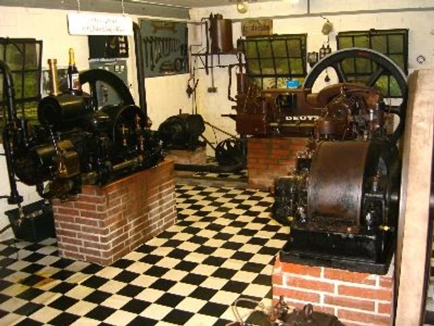 Motorenmuseum der Familie Pott Historische Motoren auf gemustertem Boden, umgeben von Maschinen und Werkzeugen im Museum der Familie Pott.