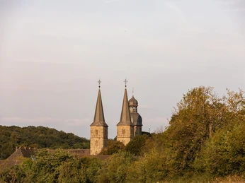 Zwei historische Kirchtürme ragen über herbstlichen Bäumen in einer malerischen Landschaft empor.