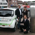 Ladesäule für Elektroautos und -roller Drei Personen präsentieren ein Elektroauto an einer Ladestation in einer urbanen Umgebung.