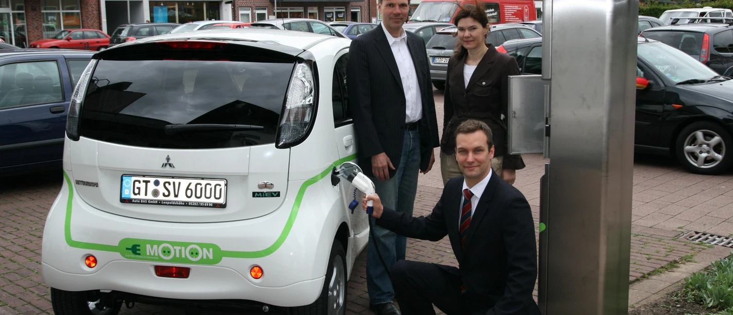 Ladesäule für Elektroautos und -roller Drei Personen präsentieren ein Elektroauto an einer Ladestation in einer urbanen Umgebung.