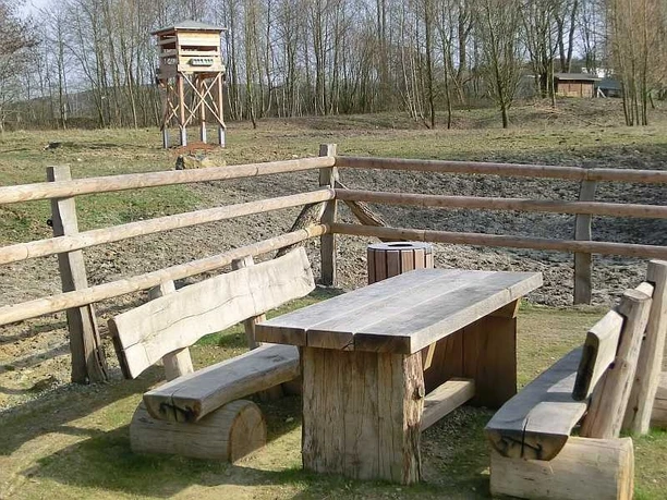 Picknickplatz an den Nieheimer Tongruben Picknickplatz mit Holztisch und Bänken, umgeben von Holzgeländer, nahe einem Aussichtsturm im Freien.