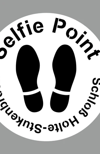Kreisförmiges Schild mit der Aufschrift "Selfie Point Schloss Holte-Stukenbrock", darunter Fußabdrücke.