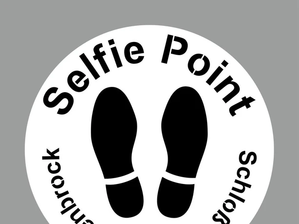 Kreisförmiges Schild mit der Aufschrift "Selfie Point Schloss Holte-Stukenbrock", darunter Fußabdrücke.
