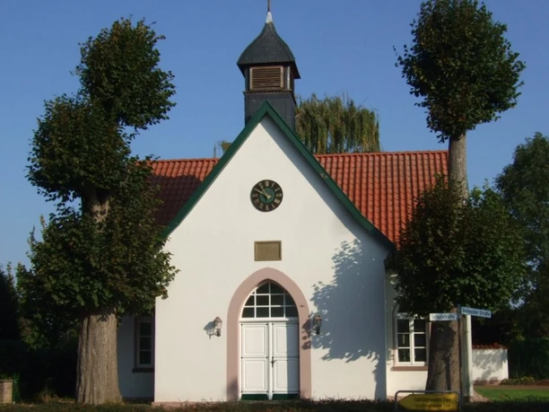 Alte Schule am Dorfplatz Getmold Weißes Gebäude mit rotem Ziegeldach und kleiner Glockenturm in Getmold, flankiert von Bäumen.