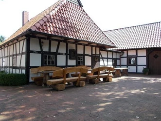 Altes Backhaus Heddinghausen Fachwerkgebäude mit roten Ziegeldach, Holz-Sitzbänken und Tischen auf gepflastertem Vorplatz.
