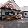 Altes Backhaus Heddinghausen Fachwerkgebäude mit roten Ziegeldach, Holz-Sitzbänken und Tischen auf gepflastertem Vorplatz.