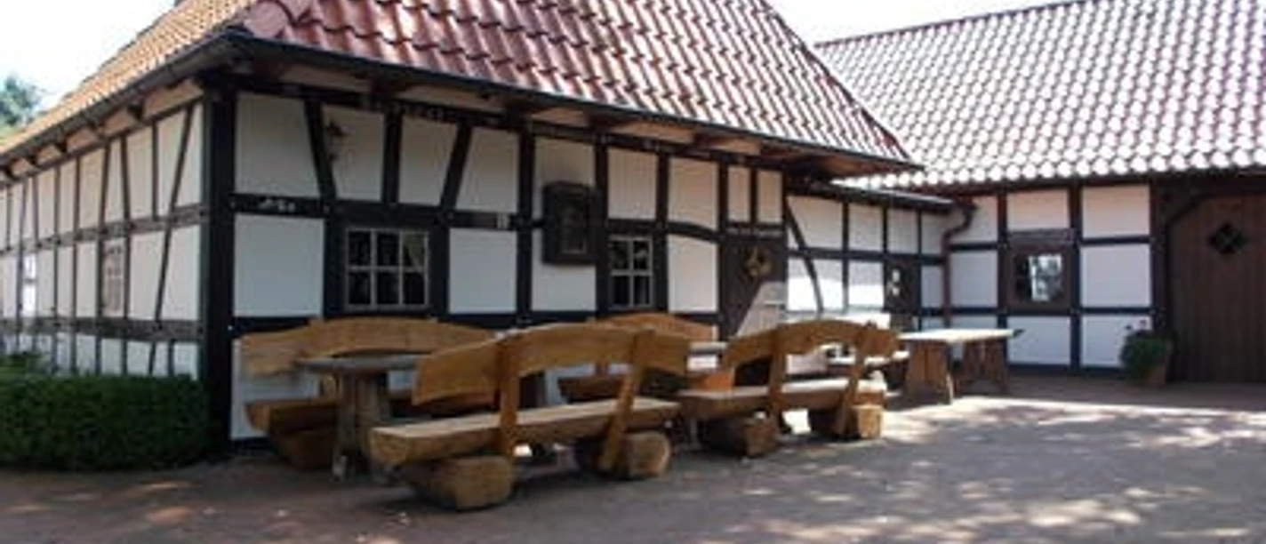 Altes Backhaus Heddinghausen Fachwerkgebäude mit roten Ziegeldach, Holz-Sitzbänken und Tischen auf gepflastertem Vorplatz.