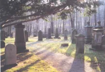 Gräber und Denkmäler unter Bäumen in ruhiger Waldlichtung im Jüdischen Friedhof Preußisch Oldendorf.