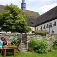 Garten in der Klosteranlage Ein Klostergarten mit alten Steinmauern, einem Holztisch und zwei entspannenden Personen auf einer Bank.