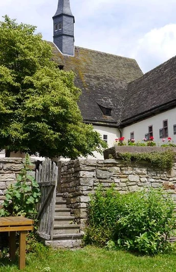 Garten in der Klosteranlage Ein Klostergarten mit alten Steinmauern, einem Holztisch und zwei entspannenden Personen auf einer Bank.