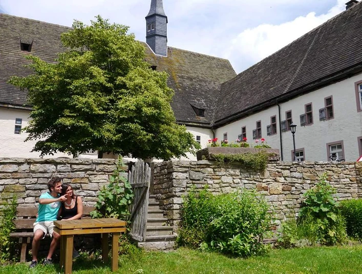 Garten in der Klosteranlage Ein Klostergarten mit alten Steinmauern, einem Holztisch und zwei entspannenden Personen auf einer Bank.