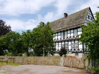 Historisches Fachwerkhaus mit schwarz-weißen Fassadenelementen, umgeben von Bäumen und Steinmauer.