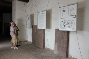 Ausstellung zur Klostergeschichte in der Klosterkirche Besucher betrachten Informationstafeln zur Klostergeschichte an einer steinernen Wand in einer Ausstellung.