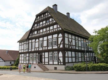 Das Priorhaus am Kloster Falkenhagen Fachwerkhaus mit steilem Satteldach und Sprossenfenstern, umgeben von Gehwegen und Vegetation.