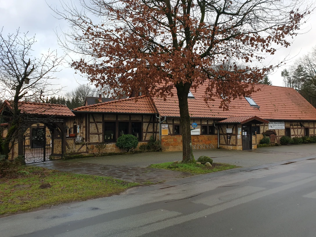 Kaffee Hexenbrink Fachwerkhaus mit rotem Dach und Steinmauer, umgeben von kahlen Bäumen, an einer asphaltierten Straße.