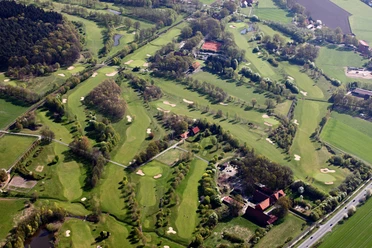 Luftaufnahme eines weitläufigen Golfplatzes mit grünen Fairways, Bunkern und umgebenden Wäldern.