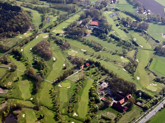 Luftaufnahme eines weitläufigen Golfplatzes mit grünen Fairways, Bunkern und umgebenden Wäldern.