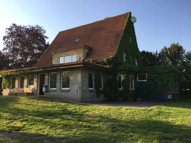 Ein zweistöckiges, mit Efeu bewachsenes Gebäude mit roten Dachziegeln im Sonnenschein.