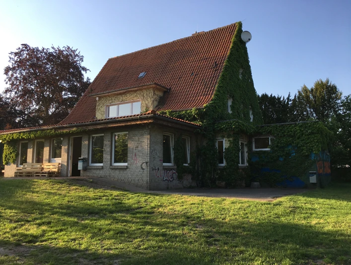 Jugendhaus "Die Villa" von hinten Ein zweistöckiges, mit Efeu bewachsenes Gebäude mit roten Dachziegeln im Sonnenschein.