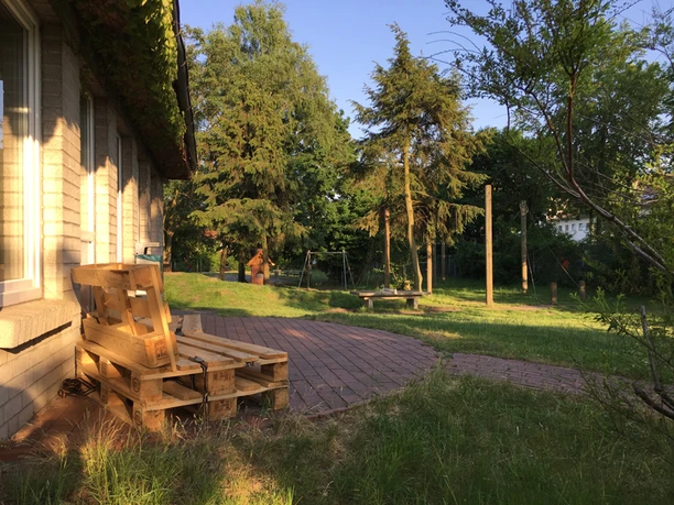 Garten mit Sonnenschein, Holzbänken aus Paletten und umgebendem Grün unter blauem Himmel.