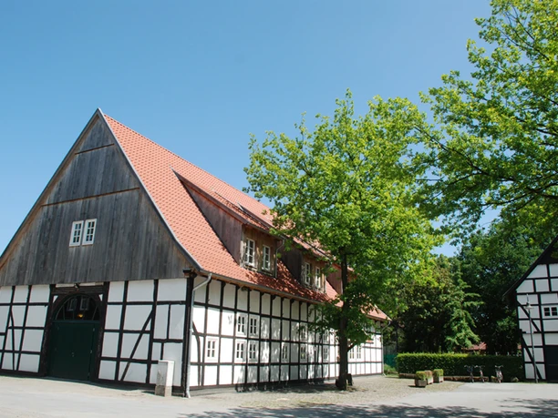 Heimathaus Harsewinkel Außenansicht Fachwerkhaus mit rotem Ziegeldach, umgeben von Bäumen, bei klarem Himmel.