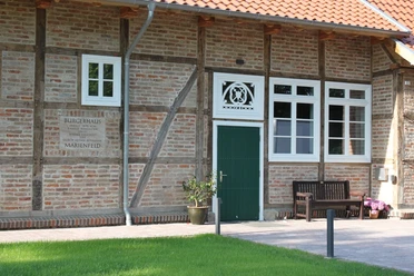 Fachwerkgebäude mit grüner Tür, Blumen und Bank davor, Schild mit "Bürgerhaus Marienfeld".