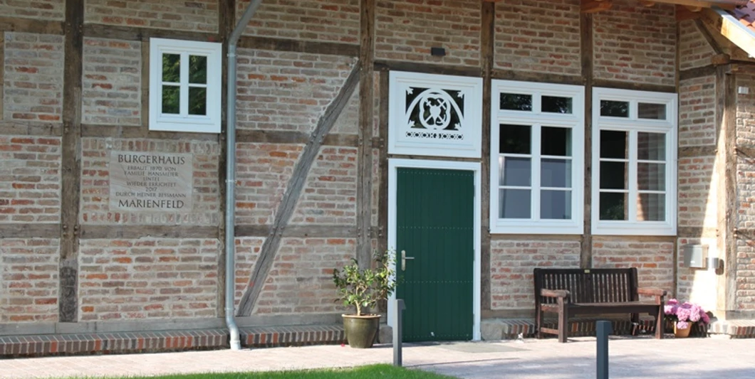 Fachwerkgebäude mit grüner Tür, Blumen und Bank davor, Schild mit "Bürgerhaus Marienfeld".