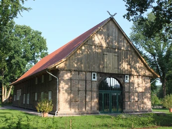 Historisches Fachwerkhaus mit Backsteinmauern und rotem Satteldach, von Bäumen umgeben.